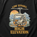 Close-up of a vintage raccoon gondola design with snowy mountains, a sunset and the words “Low Effort, High Elevation.”