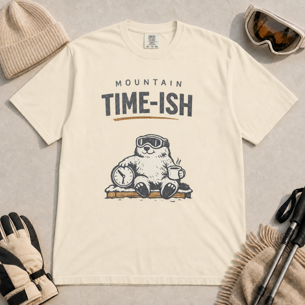 Ivory white t-shirt featuring a relaxed marmot in ski goggles holding a clock and steaming mug beneath the words “Mountain Time-ish.”