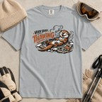 Granite gray t-shirt featuring a smiling otter thawing in a rocky hot spring beside ski goggles and a beanie.