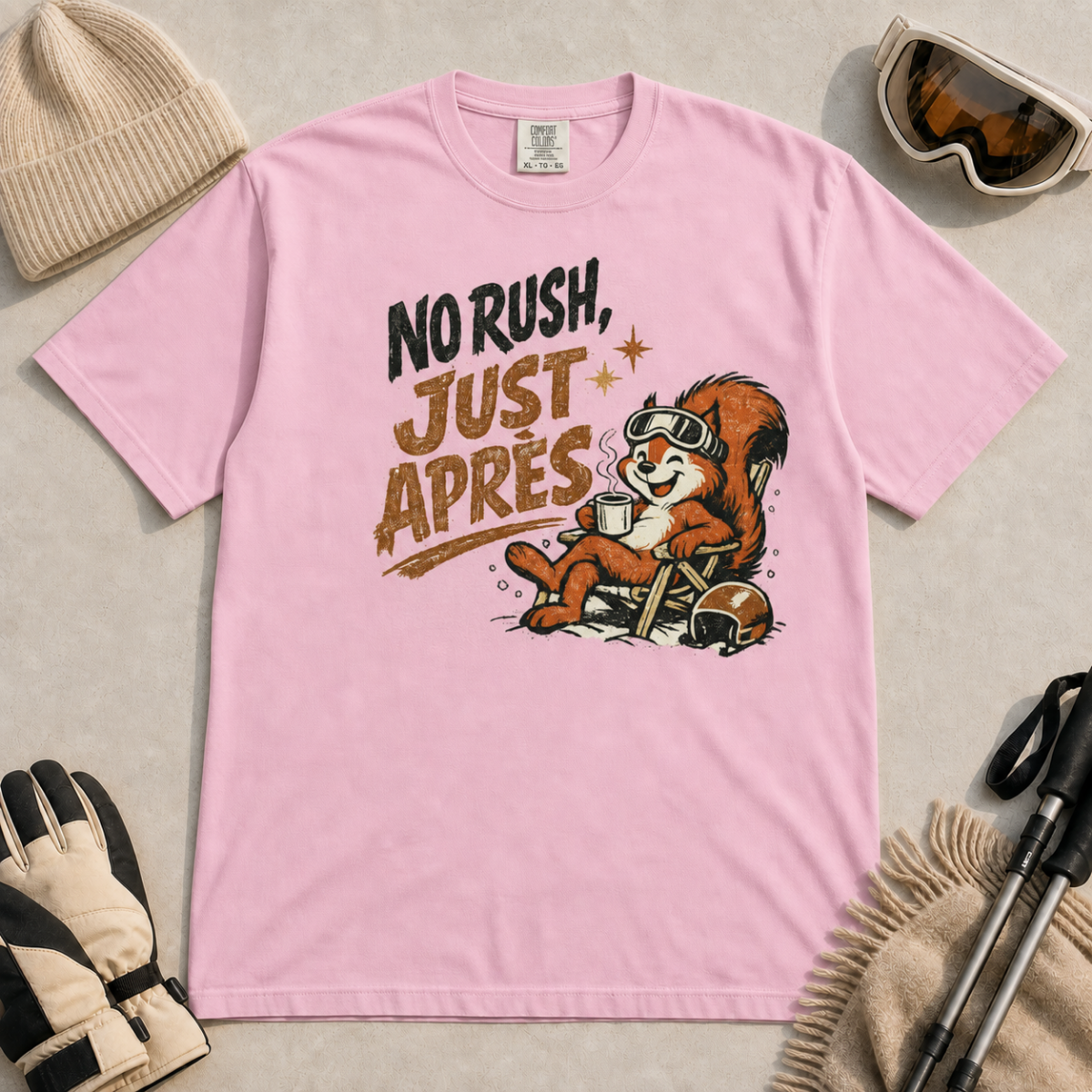 Blossom pink t-shirt featuring a relaxed red squirrel in ski goggles sitting in a chair with a steaming mug and ski helmet, beside the words “No Rush, Just Après.”