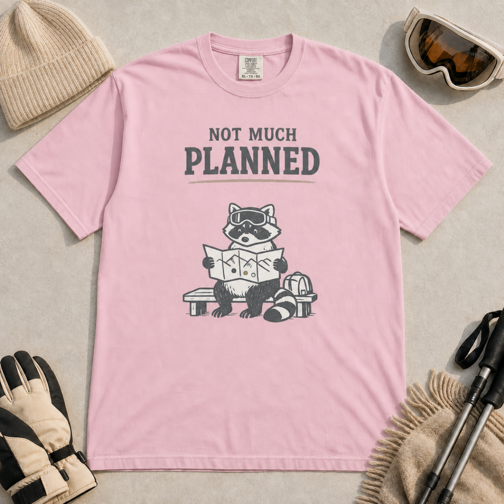 Blossom pink t-shirt featuring a raccoon in ski goggles sitting on a bench and studying a trail map, with the words “Not Much Planned.”
