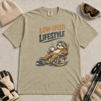Khaki t-shirt featuring a relaxed sloth in ski goggles rocking in a chair with a hot drink beneath the words “Low-Speed Lifestyle.”
