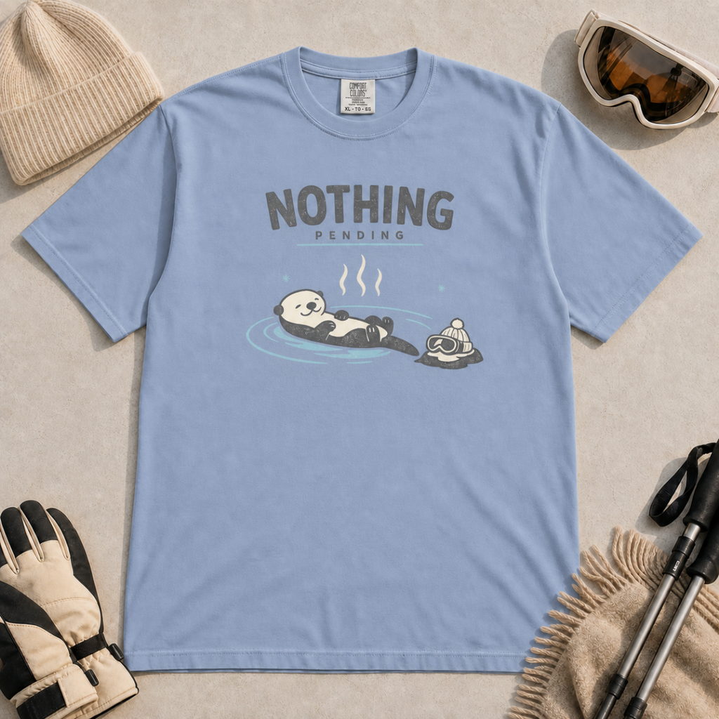 Washed denim blue t-shirt featuring a relaxed otter floating in a hot spring beside winter goggles and a beanie, with the words “Nothing Pending.”