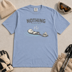 Washed denim blue t-shirt featuring a relaxed otter floating in a hot spring beside winter goggles and a beanie, with the words “Nothing Pending.”