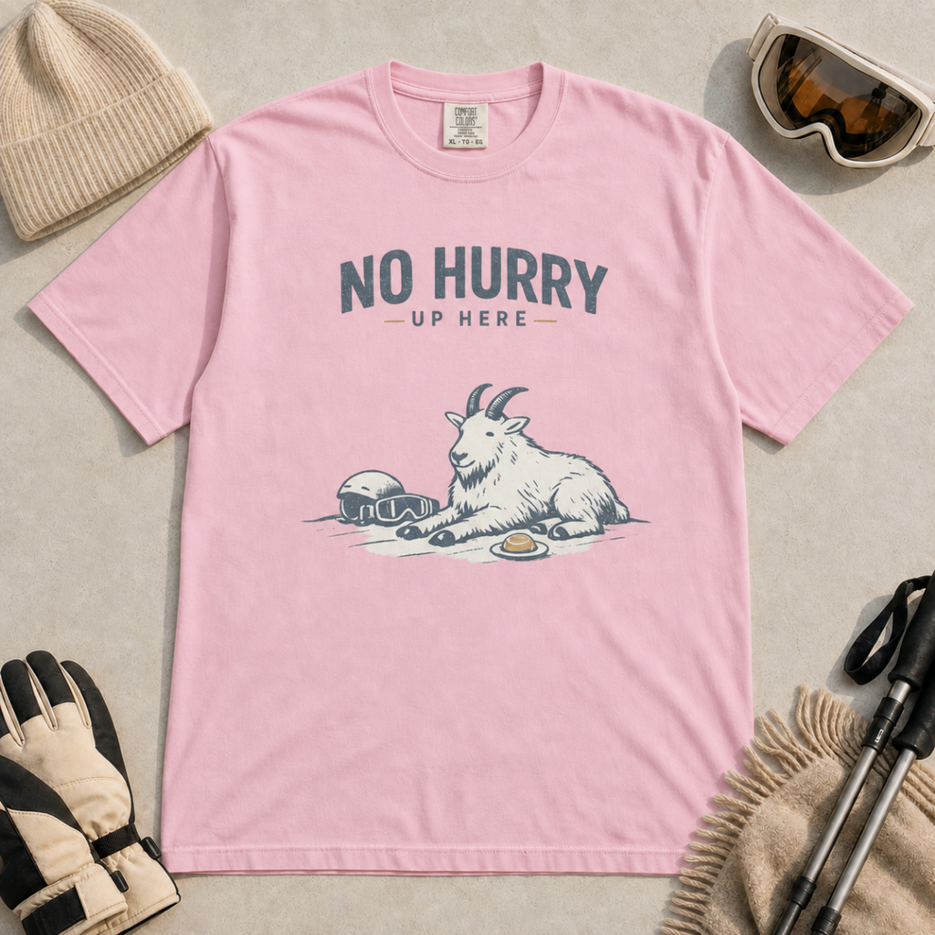 Blossom pink t-shirt featuring a mountain goat relaxing in the snow with a helmet, goggles and snack beneath the words “No Hurry Up Here.”