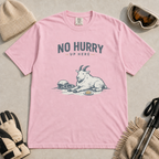 Blossom pink t-shirt featuring a mountain goat relaxing in the snow with a helmet, goggles and snack beneath the words “No Hurry Up Here.”