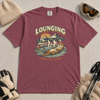 Brick red t-shirt featuring an otter relaxing in a steaming mountain hot spring beneath the words “Lounging Above Sea Level.”