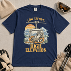 Navy t-shirt featuring a relaxed raccoon holding a mug inside a mountain gondola beneath the words “Low Effort, High Elevation.”