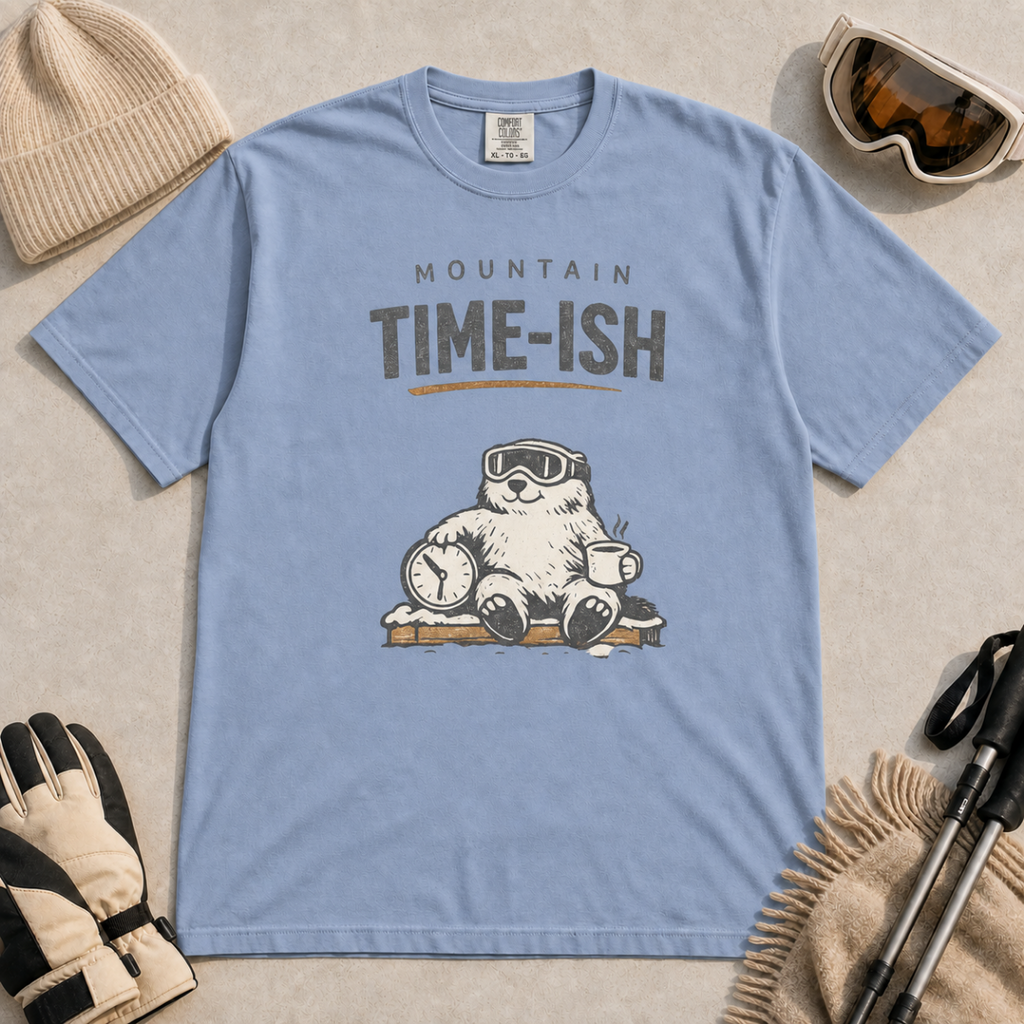 Washed denim blue t-shirt featuring a relaxed marmot in ski goggles holding a clock and steaming mug beneath the words “Mountain Time-ish.”