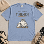 Washed denim blue t-shirt featuring a relaxed marmot in ski goggles holding a clock and steaming mug beneath the words “Mountain Time-ish.”