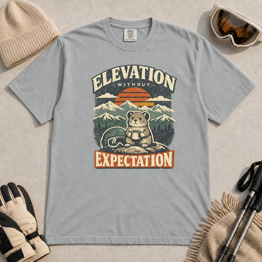 Granite grey t-shirt featuring a mountain rodent with a mug and ski goggles beneath retro sunset scenery and the phrase “Elevation Without Expectation.”
