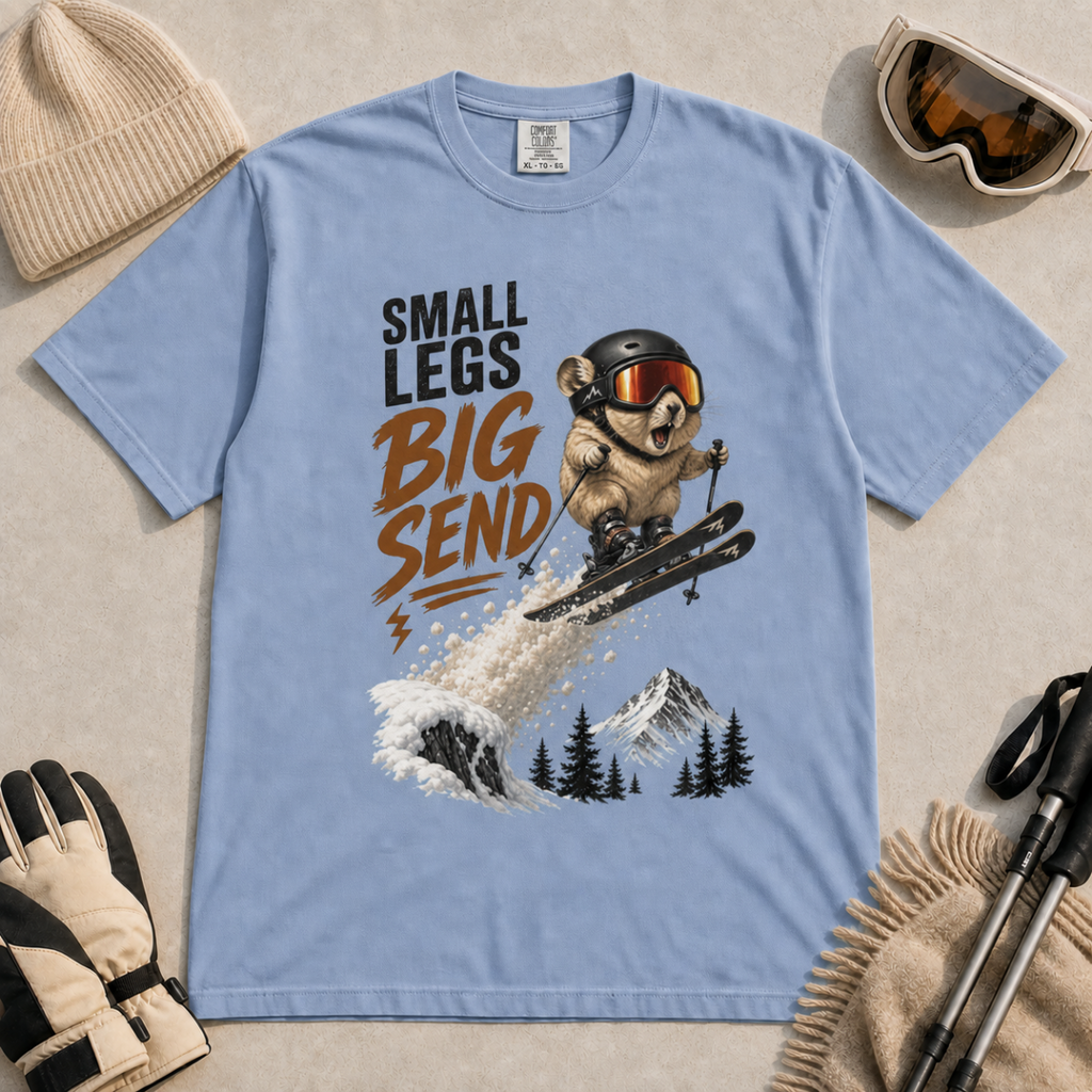 Washed denim blue t-shirt featuring a helmeted pika launching off a snowy ski jump with the phrase “Small Legs Big Send.”