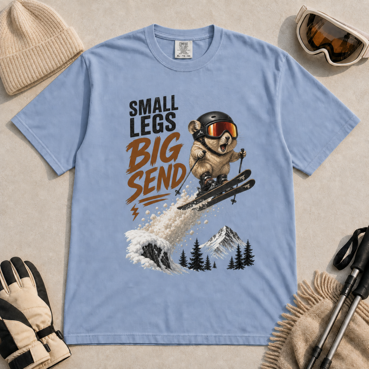 Washed denim blue t-shirt featuring a helmeted pika launching off a snowy ski jump with the phrase “Small Legs Big Send.”