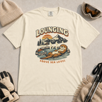 Ivory white t-shirt featuring an otter relaxing in a steaming mountain hot spring beneath the words “Lounging Above Sea Level.”
