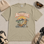 Khaki t-shirt featuring a marmot resting in a chair with a mug, ski helmet and goggles beneath “Resting Altitude” text.