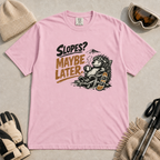Blossom pink t-shirt featuring a relaxed hedgehog in a chair with a hot drink and snowboard beneath “Slopes? Maybe Later.” text.
