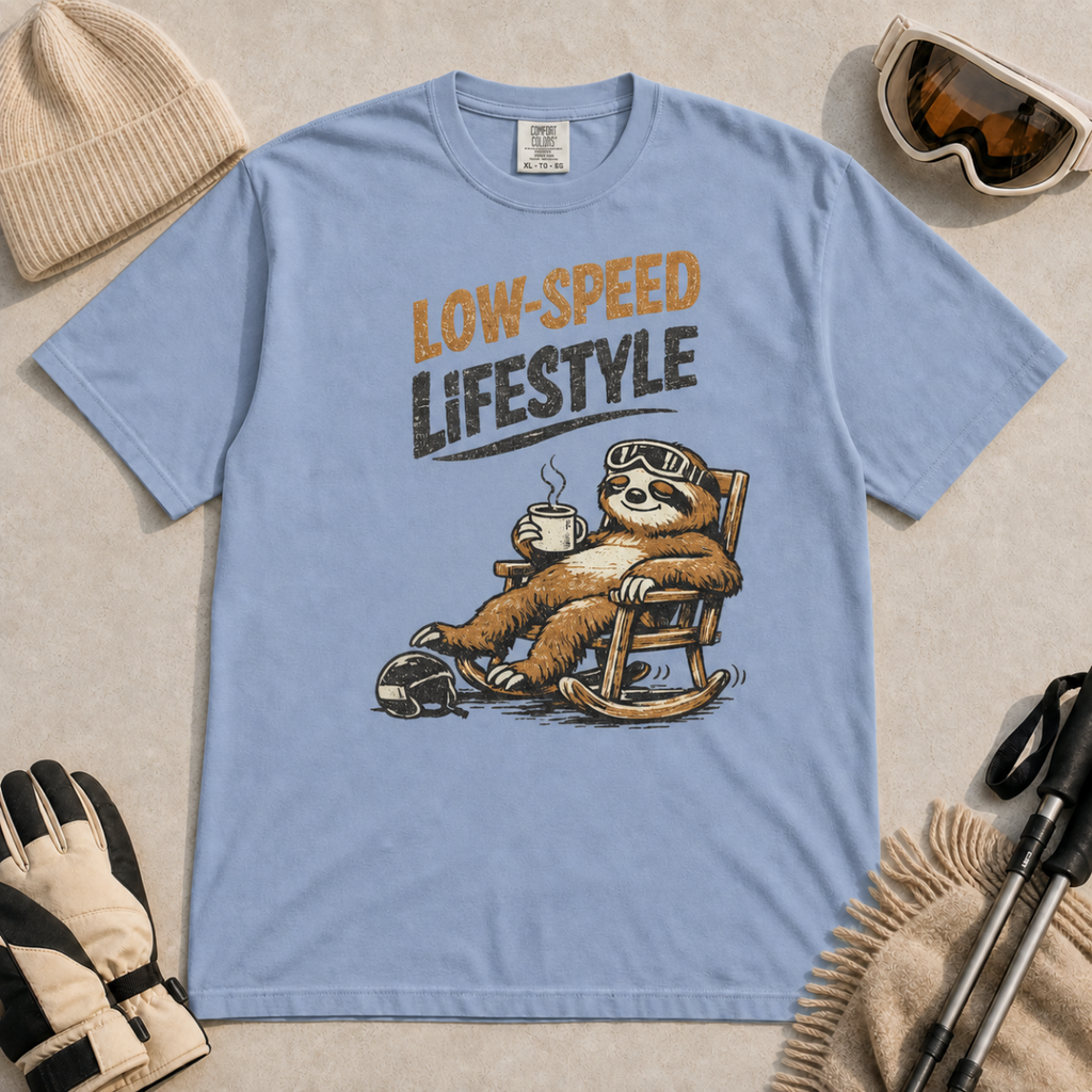 Washed denim blue t-shirt featuring a relaxed sloth in ski goggles rocking in a chair with a hot drink beneath the words “Low-Speed Lifestyle.”