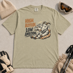 Khaki t-shirt featuring a relaxed mountain goat holding a mug beside the phrase “High Altitude, Low Ambition.”