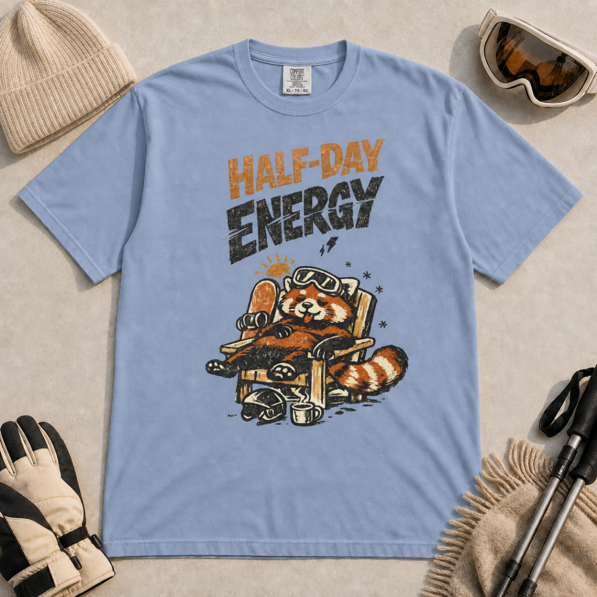 Washed denim blue t-shirt featuring a relaxed red panda in a chair beside a helmet and mug with the phrase “Half-Day Energy.”