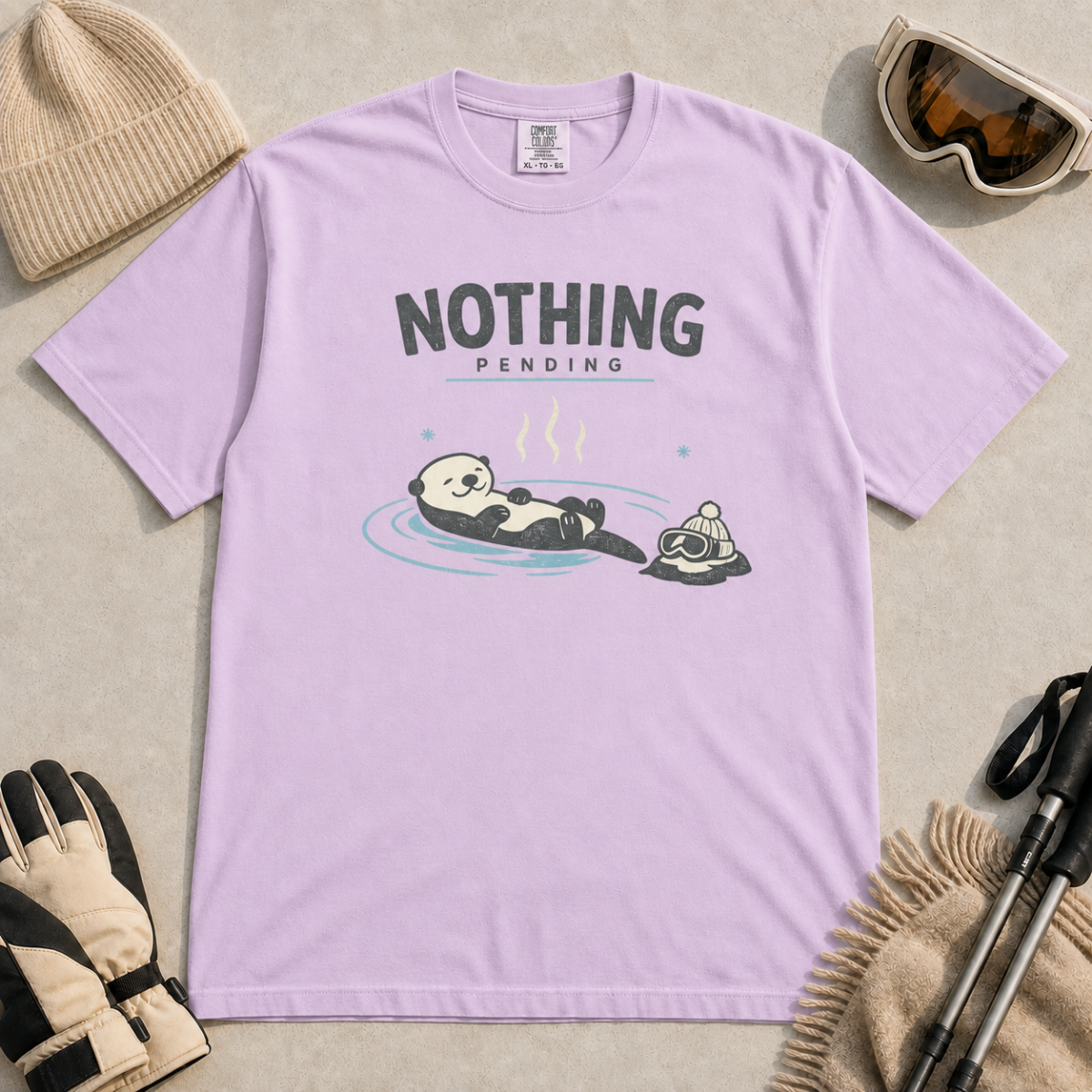Orchid purple t-shirt featuring a relaxed otter floating in a hot spring beside winter goggles and a beanie, with the words “Nothing Pending.”