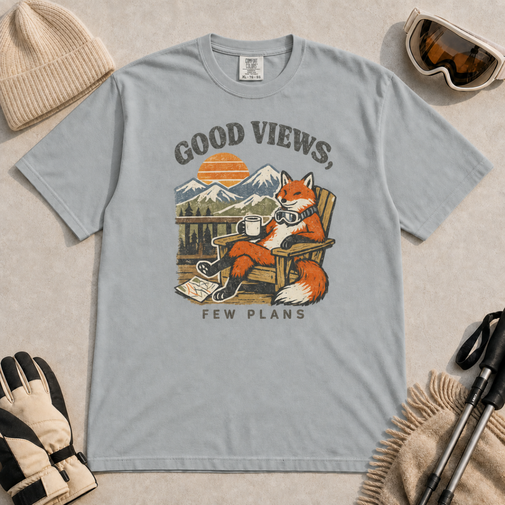 Granite gray t-shirt featuring a relaxed fox in a wooden chair holding a mug against a mountain sunset with the phrase “Good Views, Few Plans.”