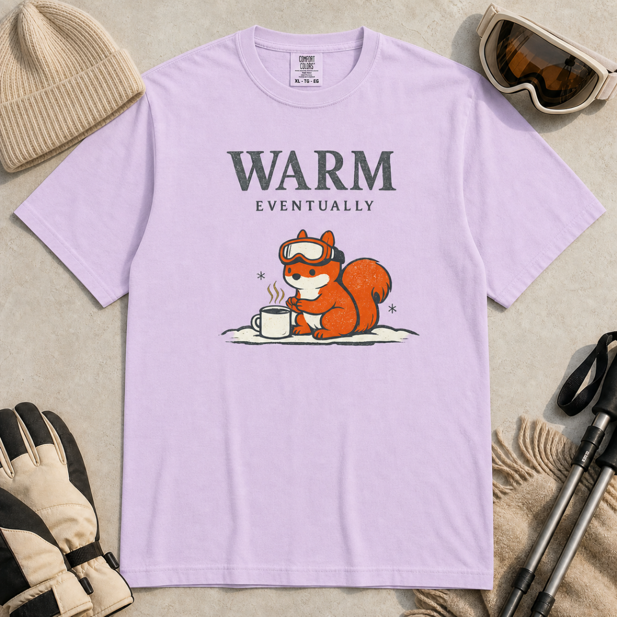 Orchid purple t-shirt featuring a bundled-up squirrel warming its paws beside a steaming mug under “Warm Eventually” text.