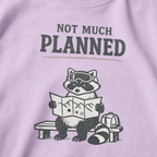 Close-up of an orchid purple t-shirt featuring a raccoon in ski goggles holding a mountain map beside a backpack, with the words “Not Much Planned.”