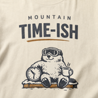 Close-up of an ivory white t-shirt design showing a relaxed marmot with ski goggles, a clock and steaming mug beneath the words “Mountain Time-ish.”