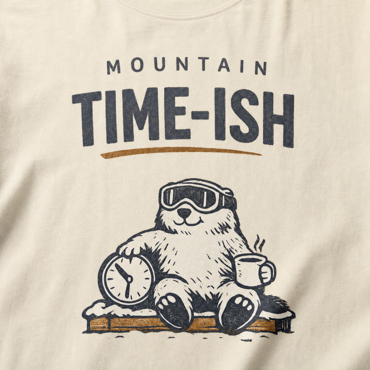 Close-up of an ivory white t-shirt design showing a relaxed marmot with ski goggles, a clock and steaming mug beneath the words “Mountain Time-ish.”