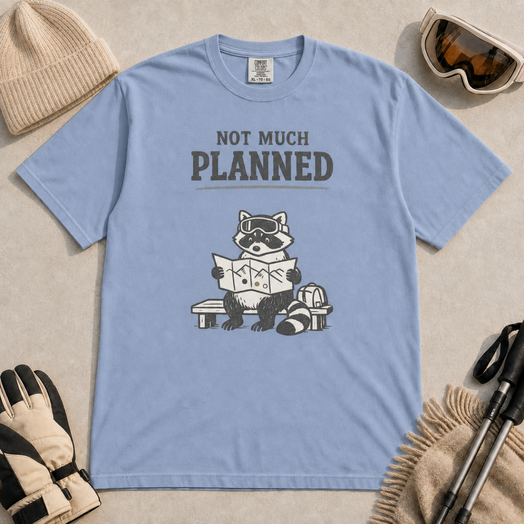 Washed denim blue t-shirt featuring a raccoon in ski goggles sitting on a bench and studying a trail map, with the words “Not Much Planned.”