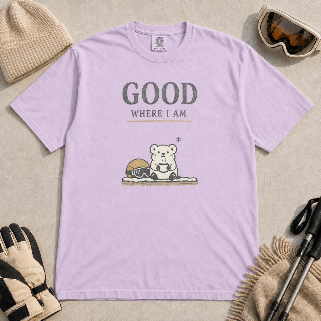 Orchid purple t-shirt featuring a small white bear holding a mug beside ski goggles with the phrase “Good Where I Am.”