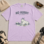 Orchid purple t-shirt featuring a mountain goat relaxing in the snow with a helmet, goggles and snack beneath the words “No Hurry Up Here.”