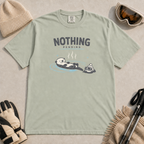 Bay green t-shirt featuring a relaxed otter floating in a hot spring beside winter goggles and a beanie, with the words “Nothing Pending.”