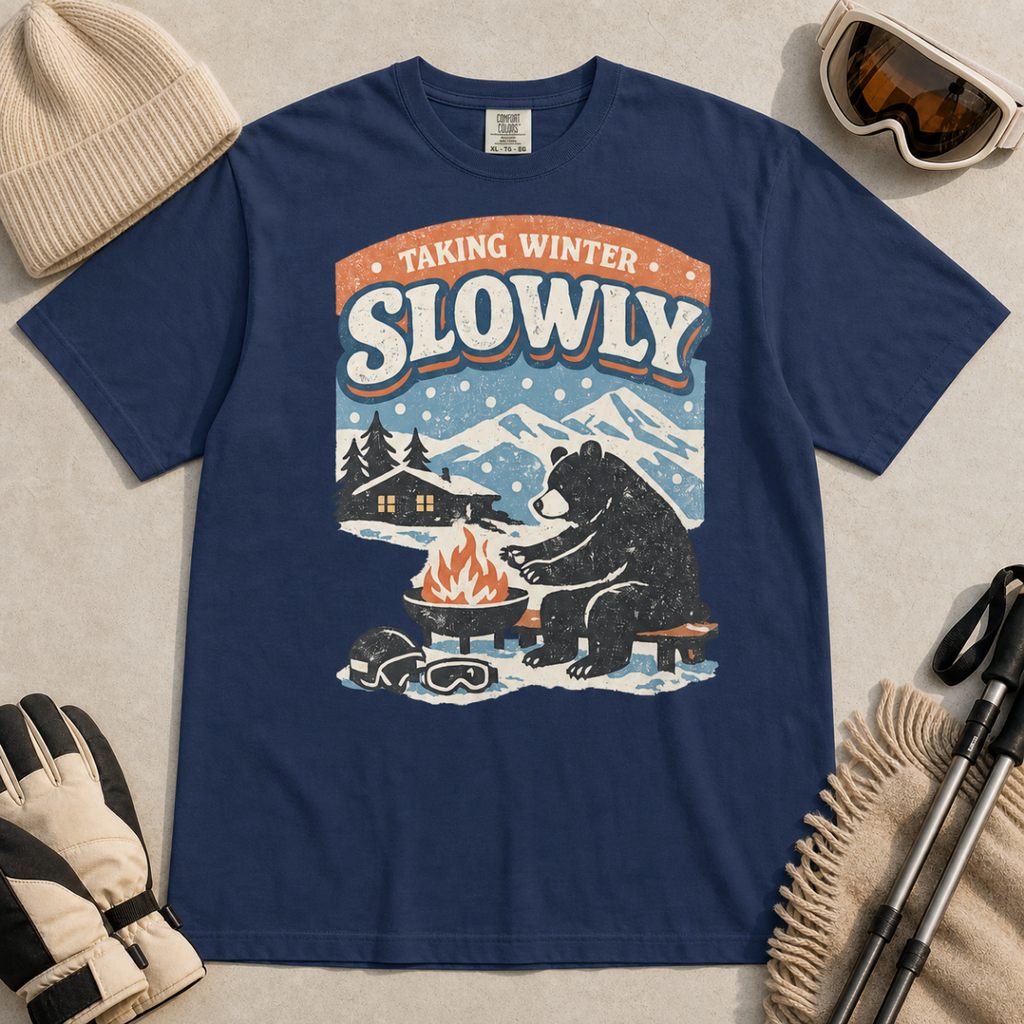 Navy blue t-shirt featuring a bear warming its paws by a fire beneath “Taking Winter Slowly” text.