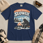 Navy blue t-shirt featuring a bear warming its paws by a fire beneath “Taking Winter Slowly” text.