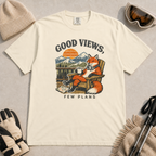 Ivory white t-shirt featuring a relaxed fox in a wooden chair holding a mug against a mountain sunset with the phrase “Good Views, Few Plans.”
