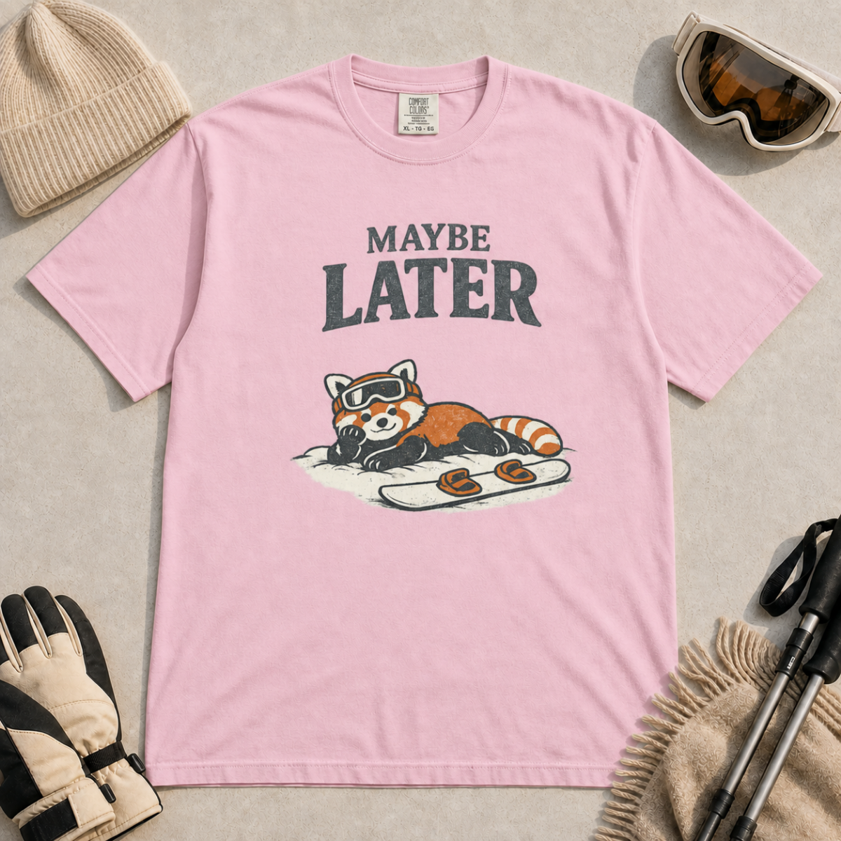 Blossom pink t-shirt featuring a relaxed red panda in ski goggles lying beside a snowboard beneath the words “Maybe Later.”