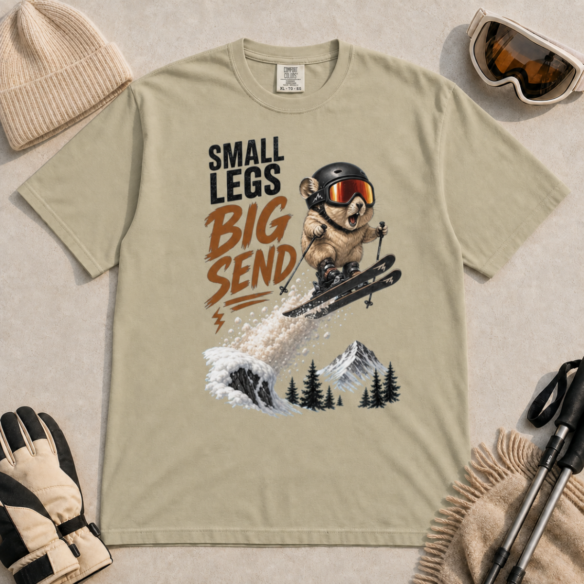 Khaki t-shirt featuring a helmeted pika launching off a snowy ski jump with the phrase “Small Legs Big Send.”