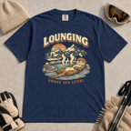 Navy t-shirt featuring an otter relaxing in a steaming mountain hot spring beneath the words “Lounging Above Sea Level.”