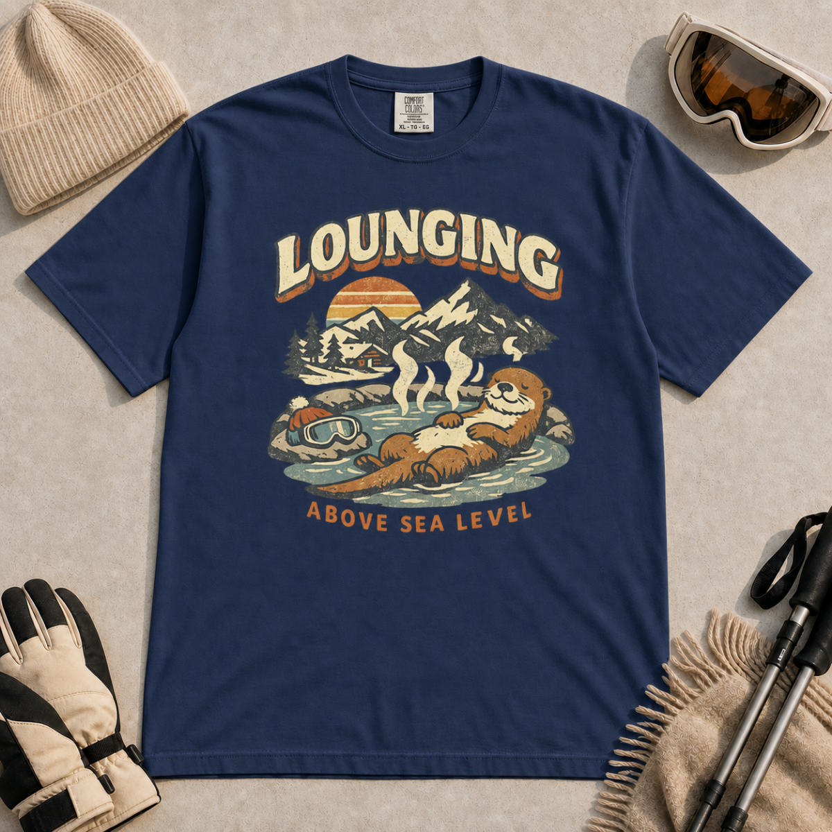 Navy t-shirt featuring an otter relaxing in a steaming mountain hot spring beneath the words “Lounging Above Sea Level.”