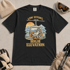 Black t-shirt featuring a relaxed raccoon holding a mug inside a mountain gondola beneath the words “Low Effort, High Elevation.”