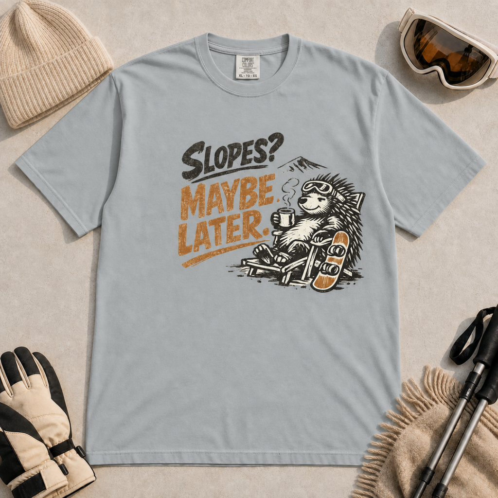 Granite gray t-shirt featuring a relaxed hedgehog in a chair with a hot drink and snowboard beneath “Slopes? Maybe Later.” text.