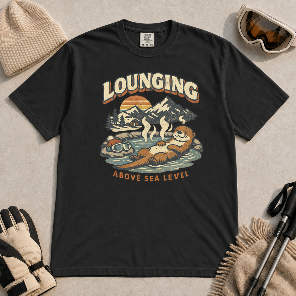 Black t-shirt featuring an otter relaxing in a steaming mountain hot spring beneath the words “Lounging Above Sea Level.”