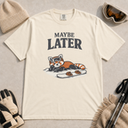 Ivory white t-shirt featuring a relaxed red panda in ski goggles lying beside a snowboard beneath the words “Maybe Later.”