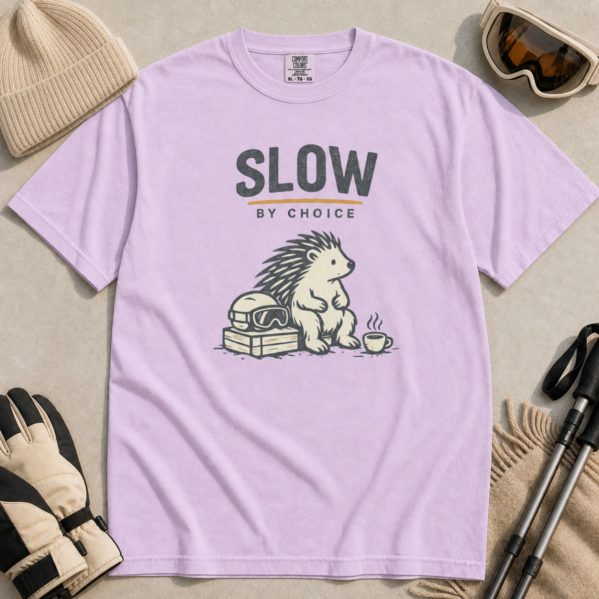 Orchid purple t-shirt featuring a seated hedgehog beside ski goggles and a hot drink beneath “Slow by Choice” text.