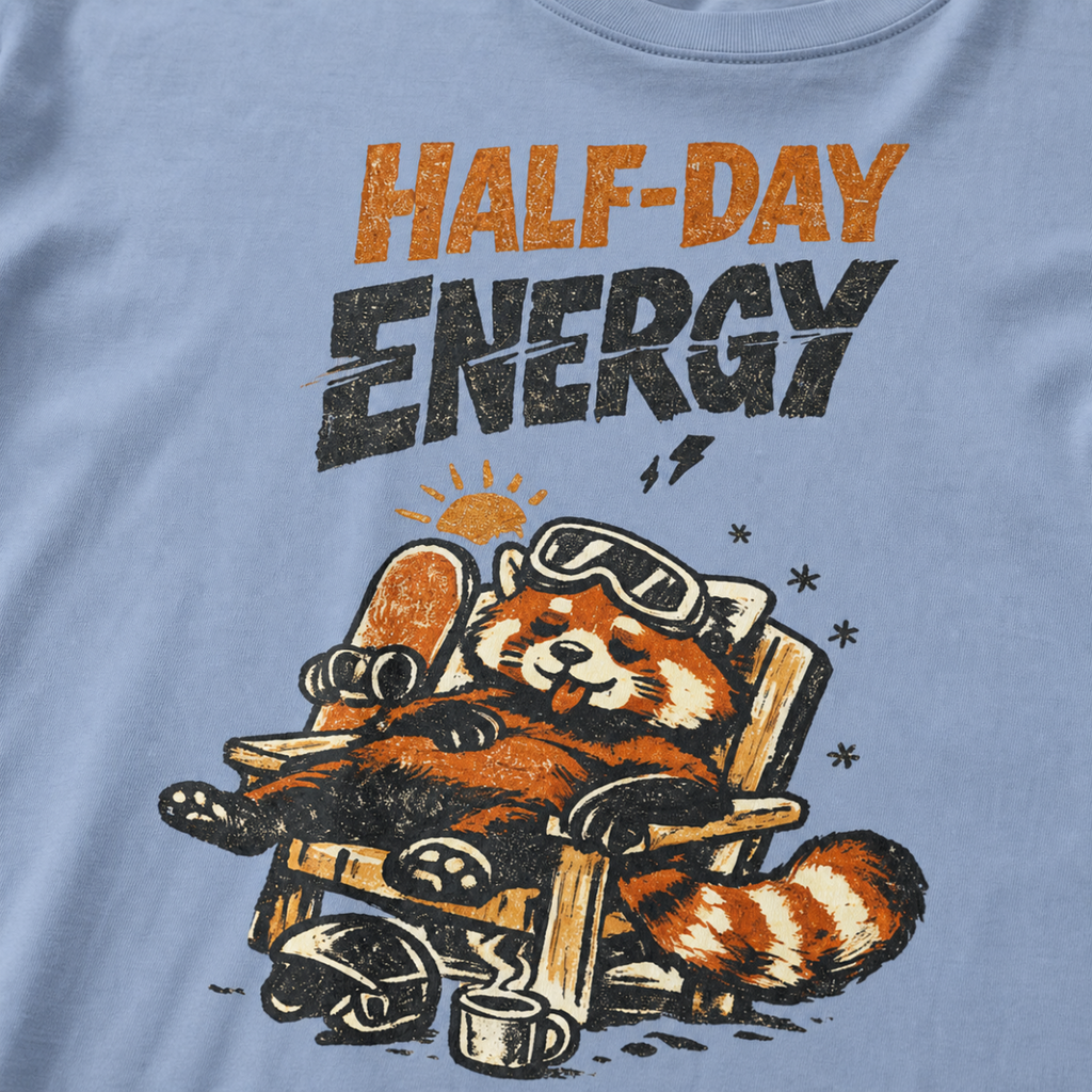 Close-up of a washed denim blue t-shirt featuring a sleepy red panda lounging in a chair with the phrase “Half-Day Energy.”