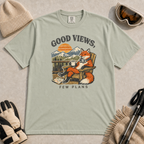 Bay green t-shirt featuring a relaxed fox in a wooden chair holding a mug against a mountain sunset with the phrase “Good Views, Few Plans.”