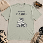 Khaki t-shirt featuring a raccoon in ski goggles sitting on a bench and studying a trail map, with the words “Not Much Planned.”