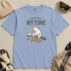 Washed denim blue t-shirt featuring a beaver seated on a bench fastening snowboard boots beneath “Taking My Time” text.