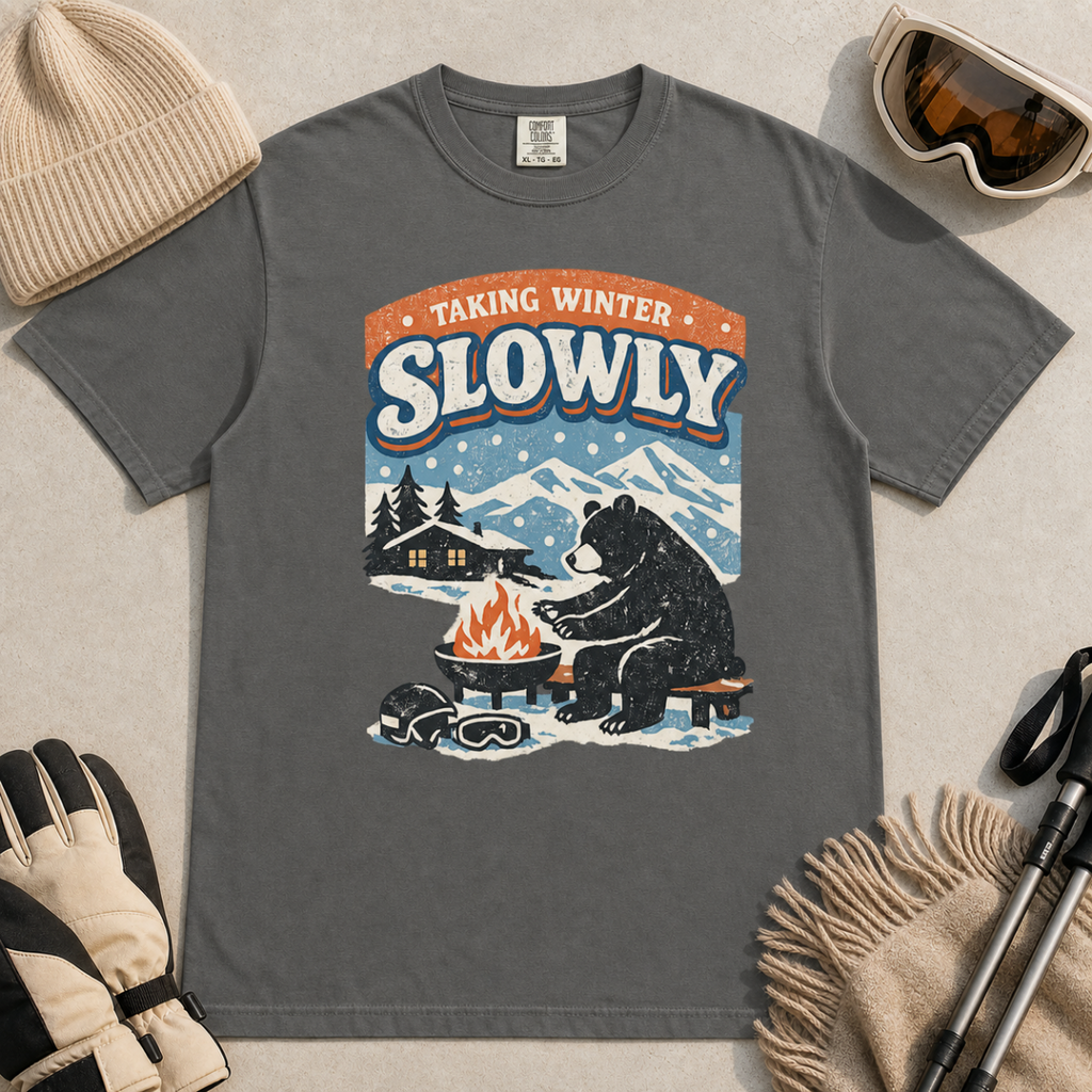 Pepper gray t-shirt featuring a bear warming its paws by a fire beneath “Taking Winter Slowly” text.